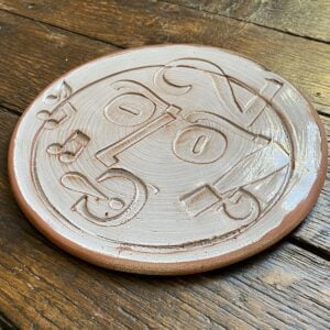 Round plate with letterpress blocks impressed into the clay to make a face. By John Ingledew.