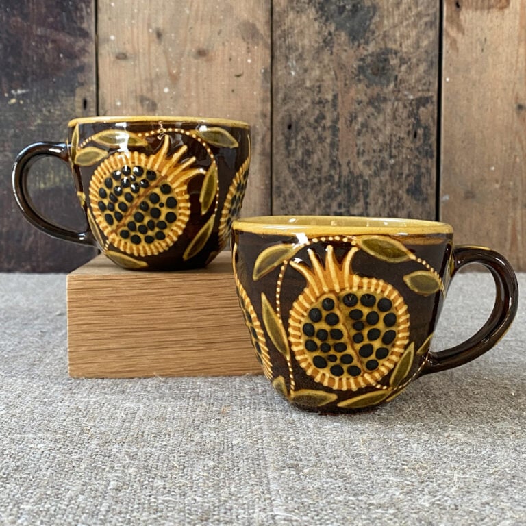 Pair of slipware mugs by Carole Glover on a linen cloth and a wooden background.