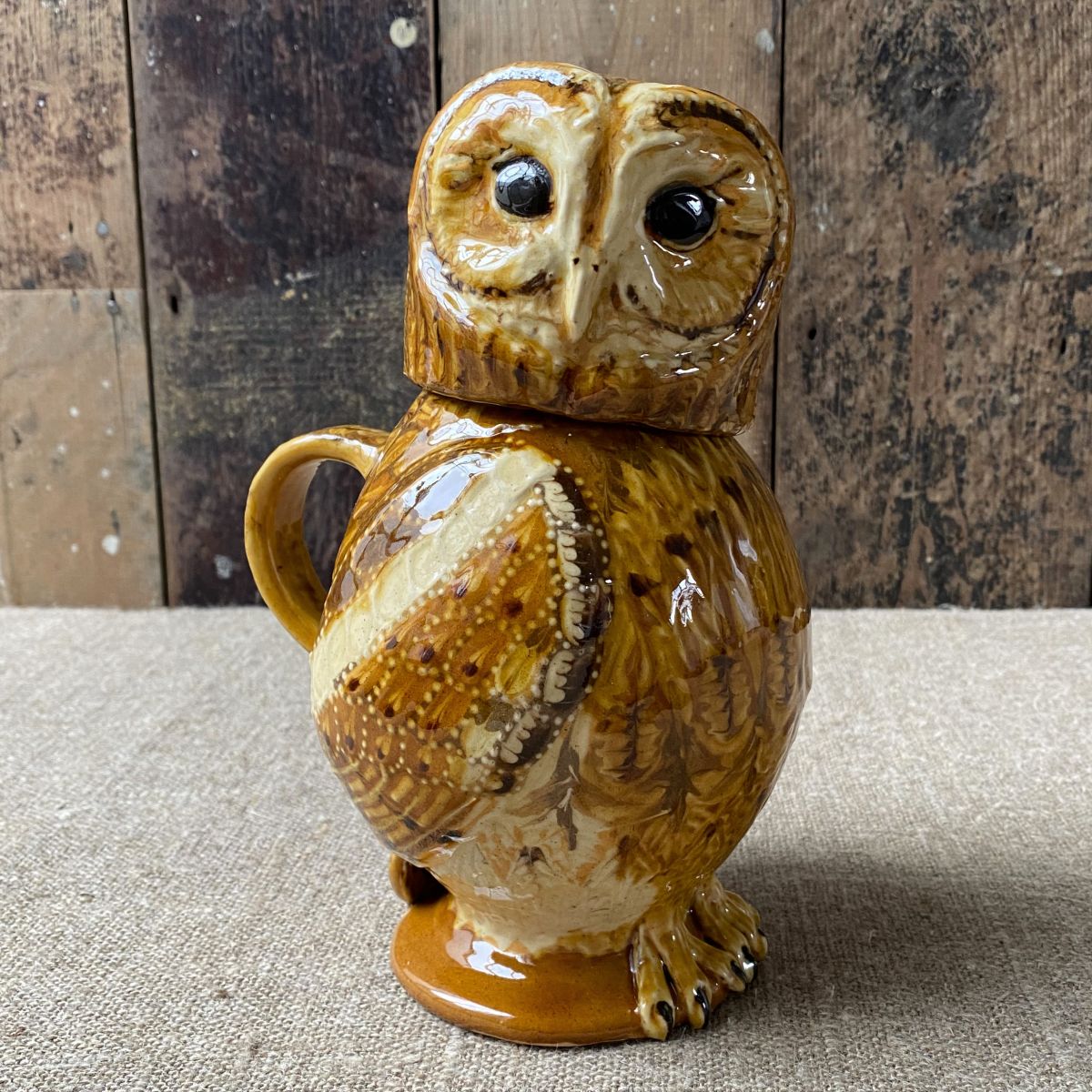 Carole Glover slipware glazed Owl Jug against a wooden background