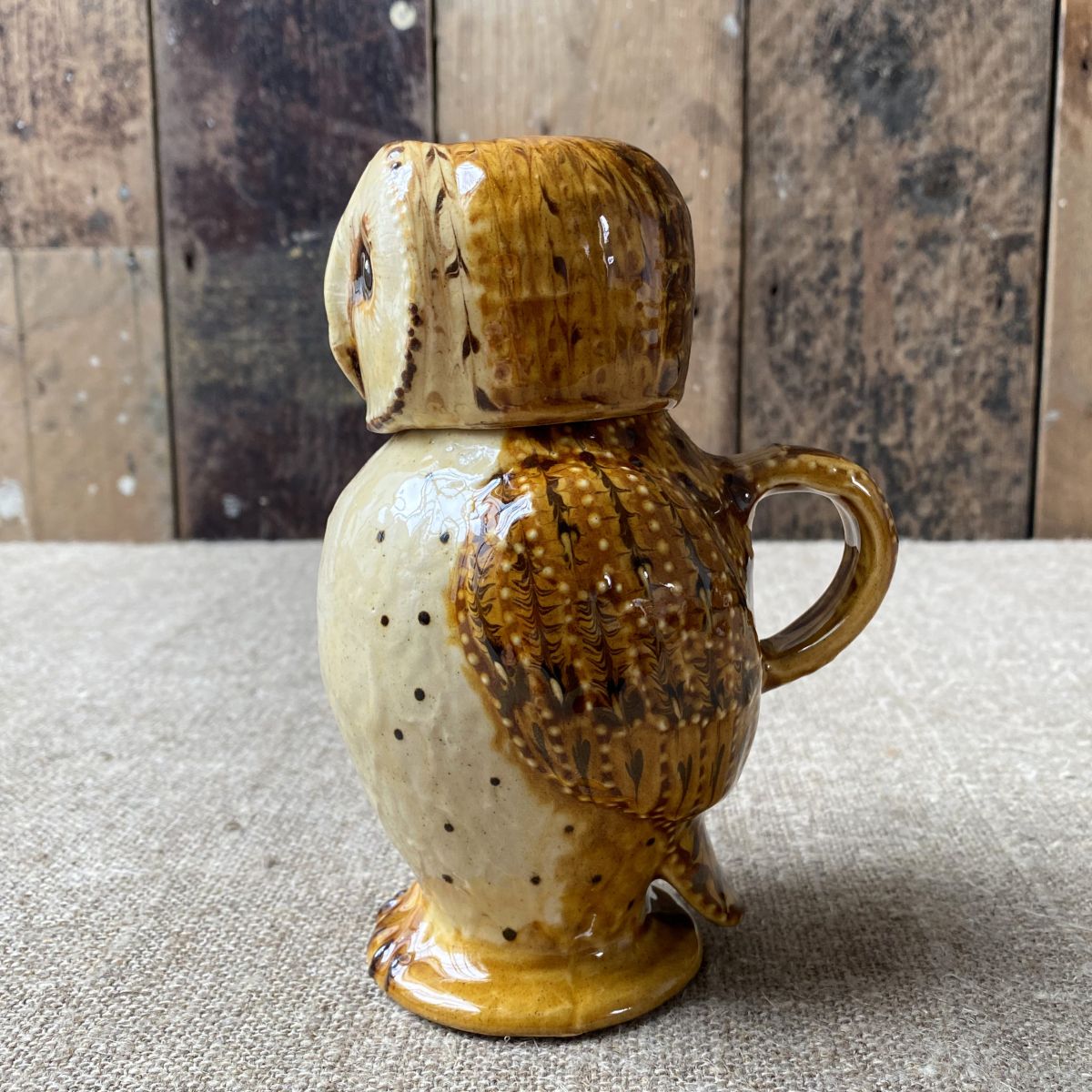 Carole Glover slipware glazed Owl Jug against a wooden background