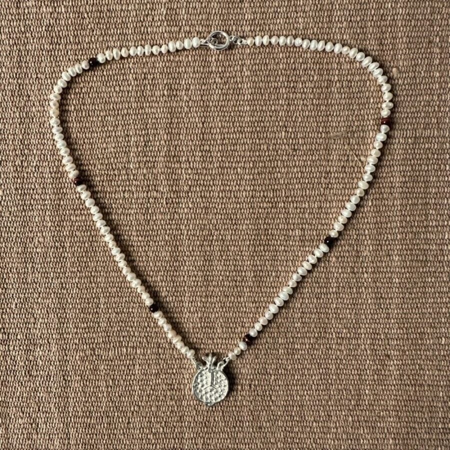 A seed pearl and red tigers eye necklace with a cast silver pomegranate pendant. Clare de la Torre.