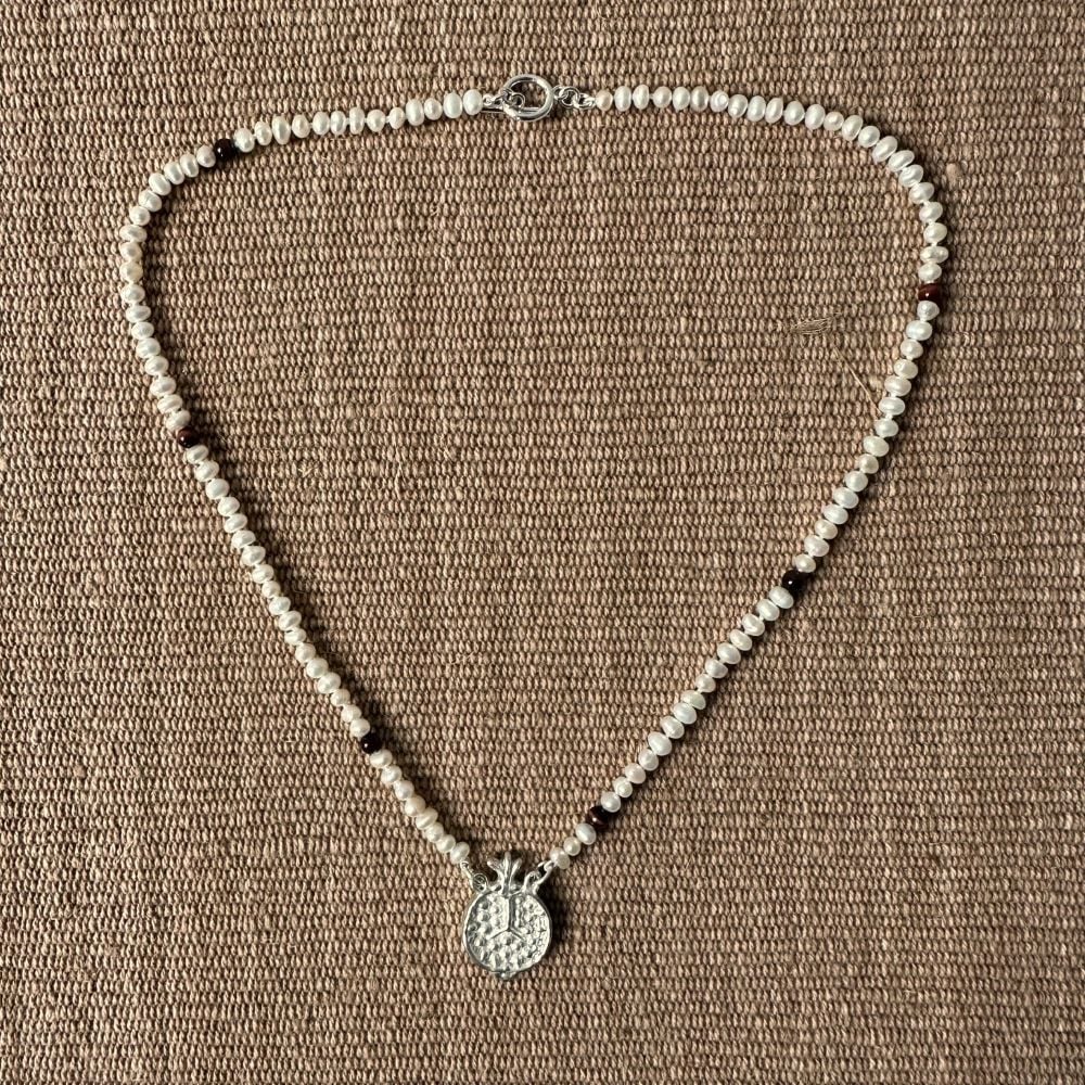 A seed pearl and red tigers eye necklace with a cast silver pomegranate pendant. Clare de la Torre.