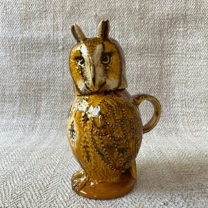 Ceramic slipware owl jug against a pale fabric background