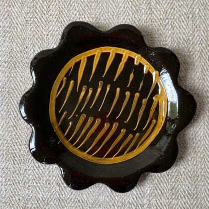 Black glazed plate with scalloped edge againsta a pale fabric background