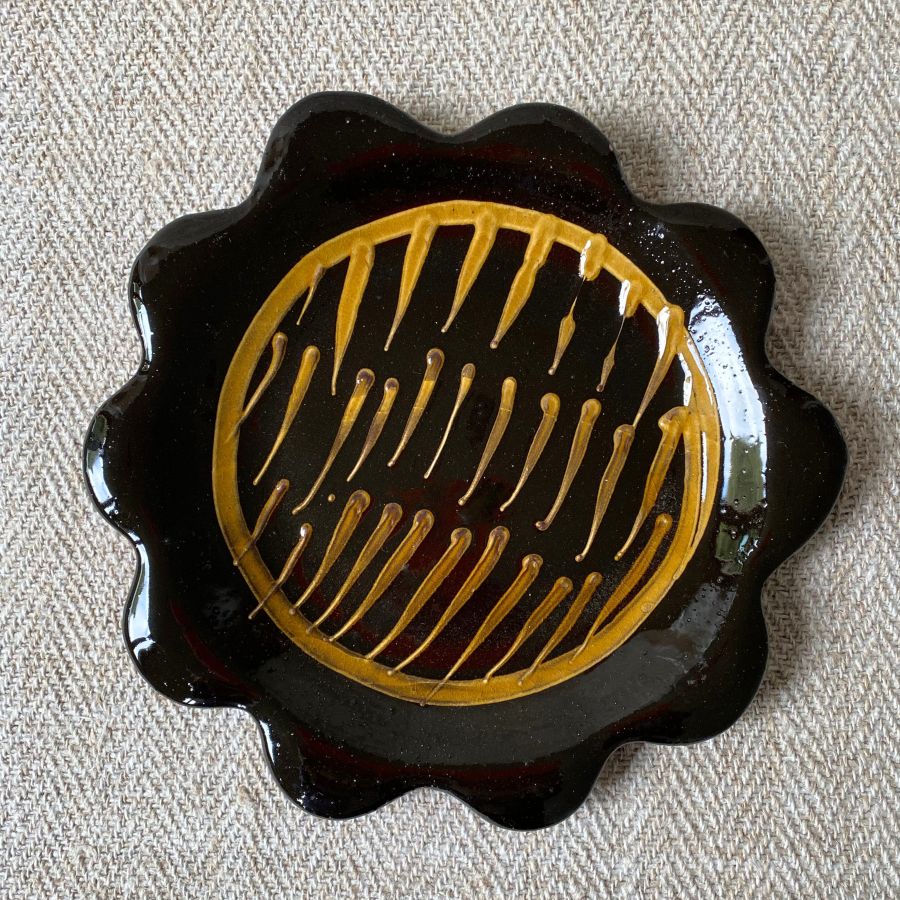 Black glazed plate with scalloped edge againsta a pale fabric background