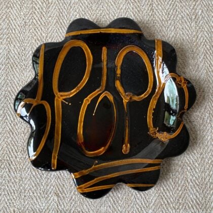 Black glazed plate with scalloped edge againsta a pale fabric background