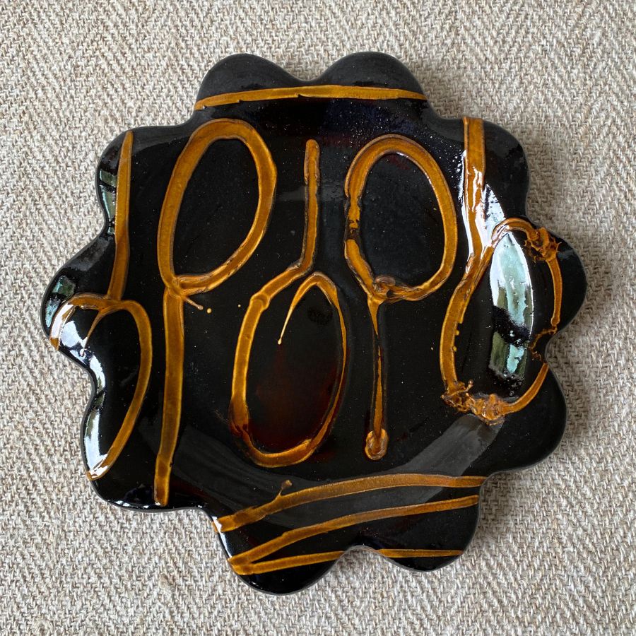 Black glazed plate with scalloped edge againsta a pale fabric background
