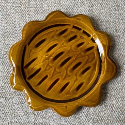 Amber glazed plate with scalloped edge againsta a pale fabric background