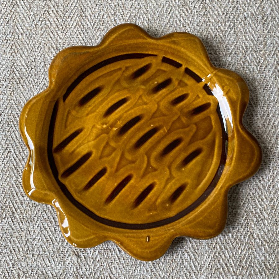 Amber glazed plate with scalloped edge againsta a pale fabric background
