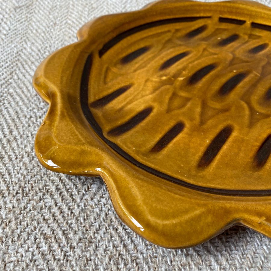 Amber glazed plate with scalloped edge againsta a pale fabric background
