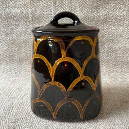 Black glazed jar with lid against a pale fabric backdrop.