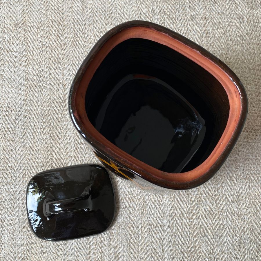 Black glazed jar with lid against a pale fabric backdrop.