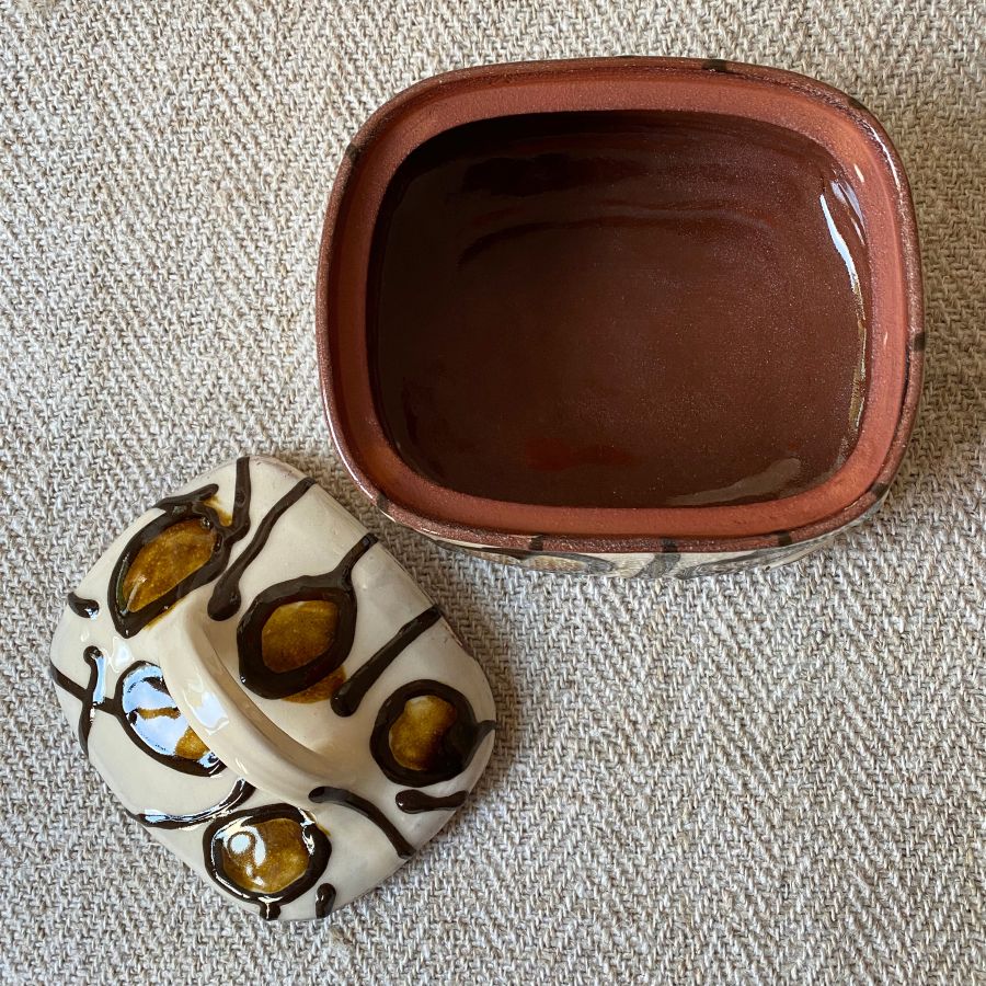 Open white glazed butter dish with lid against a fabric background