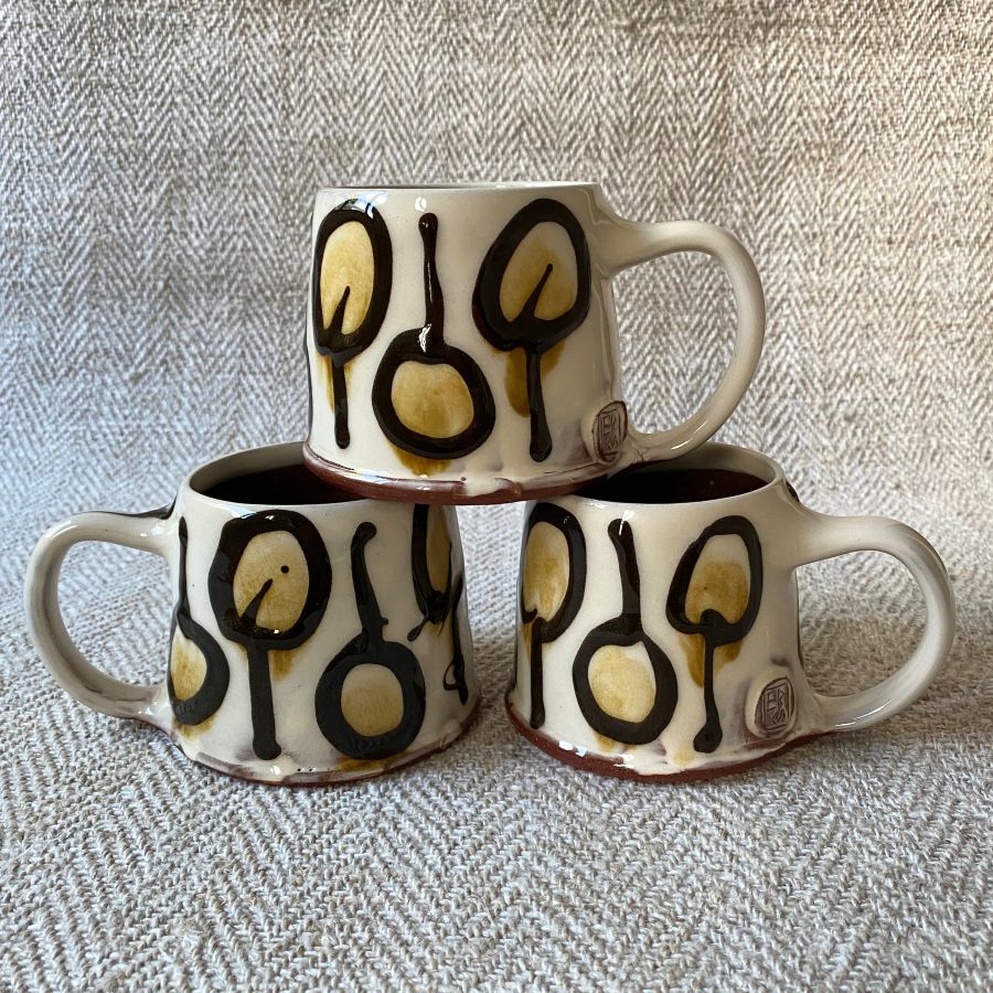 Trio of white slipware mugs against a white fabric background