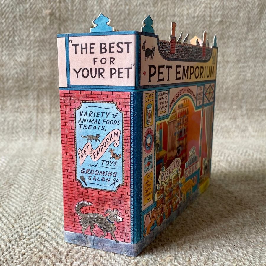 A 3D stand up card of a pet shop illustrated by Emily Sutton against a pale fabric background