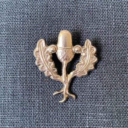 Pewter brooch in the shape of an acorn & leaves against a blue fabric background