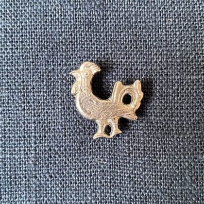 Pewter brooch in the shape of a cockerel against a blue fabric backgroun