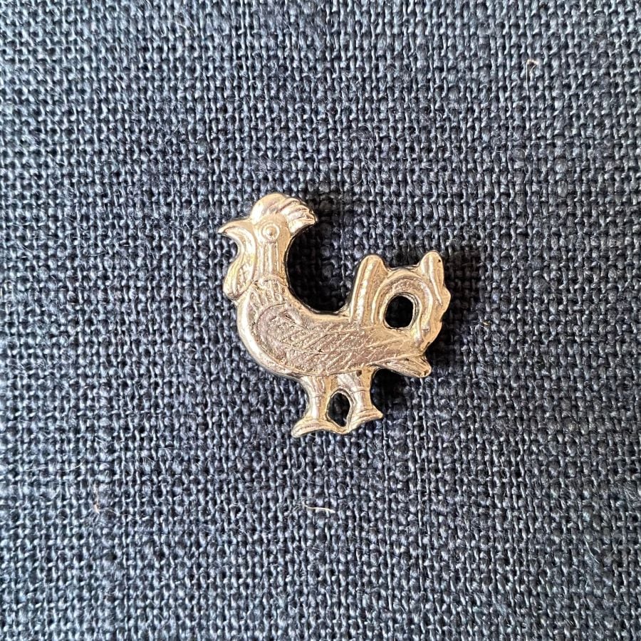 Pewter brooch in the shape of a cockerel against a blue fabric backgroun