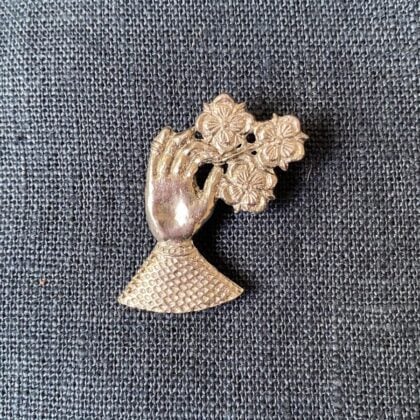 Pewter brooch in the shape of a hand against a blue fabric background
