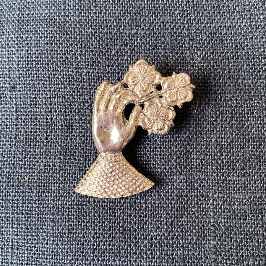 Pewter brooch in the shape of a hand against a blue fabric background