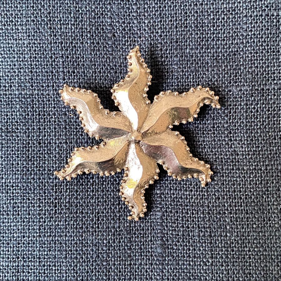 Pewter brooch in the shape of a star against a blue fabric background