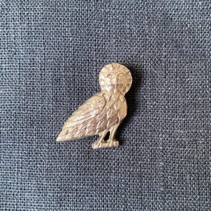 Pewter brooch in the shape of an owl against a blue fabric background