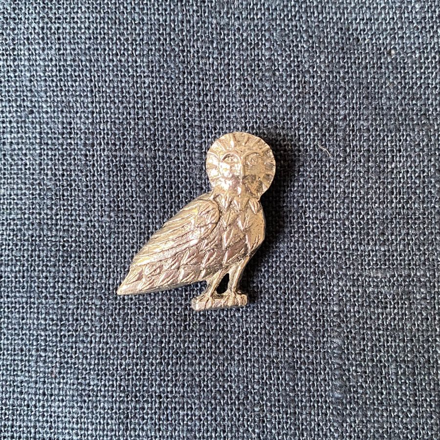 Pewter brooch in the shape of an owl against a blue fabric background